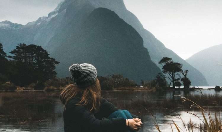 woman sitting near body of water looking at clouds