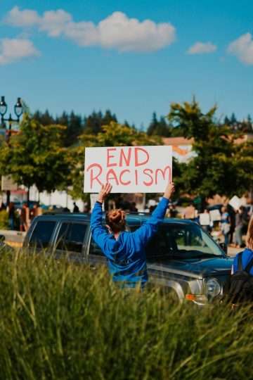 woman in blue jacket holding white and black end racism sign