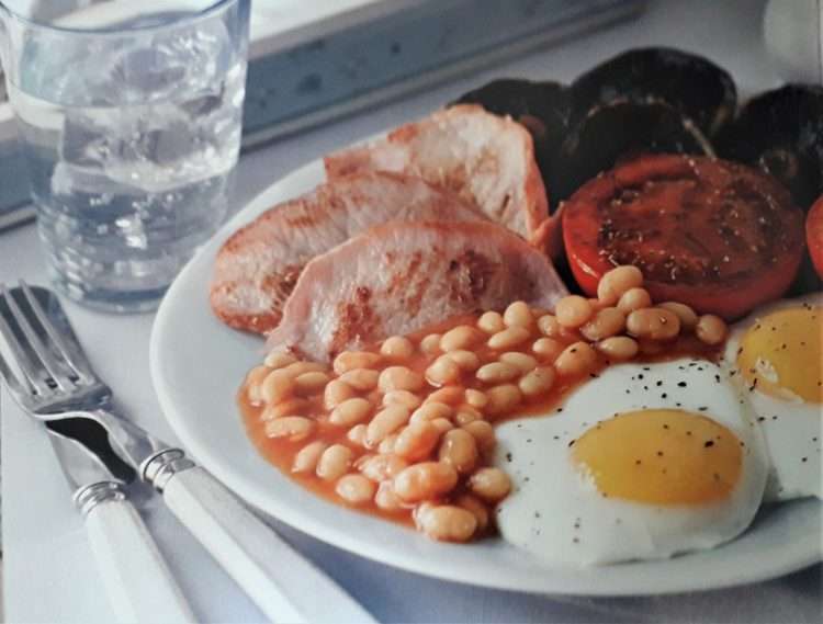 Full english breakfast|sliced bread with sliced tomato and cucumber on black ceramic plate|fruit salad on white ceramic bowl|cooked food