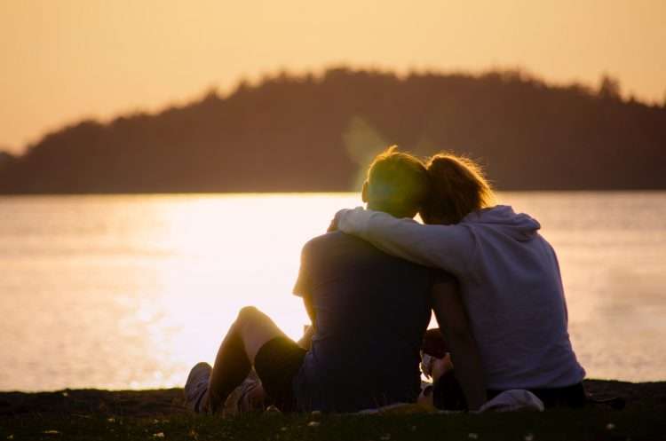 woman in black jacket sitting on green grass field near body of water at dusk