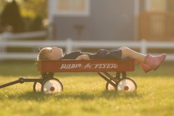 boy on red Radio Flyer pull wagon during daytime